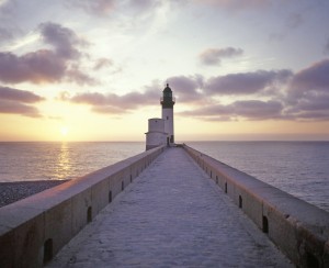 A path leading to the lighthouse is seen with sea at the background at sunset